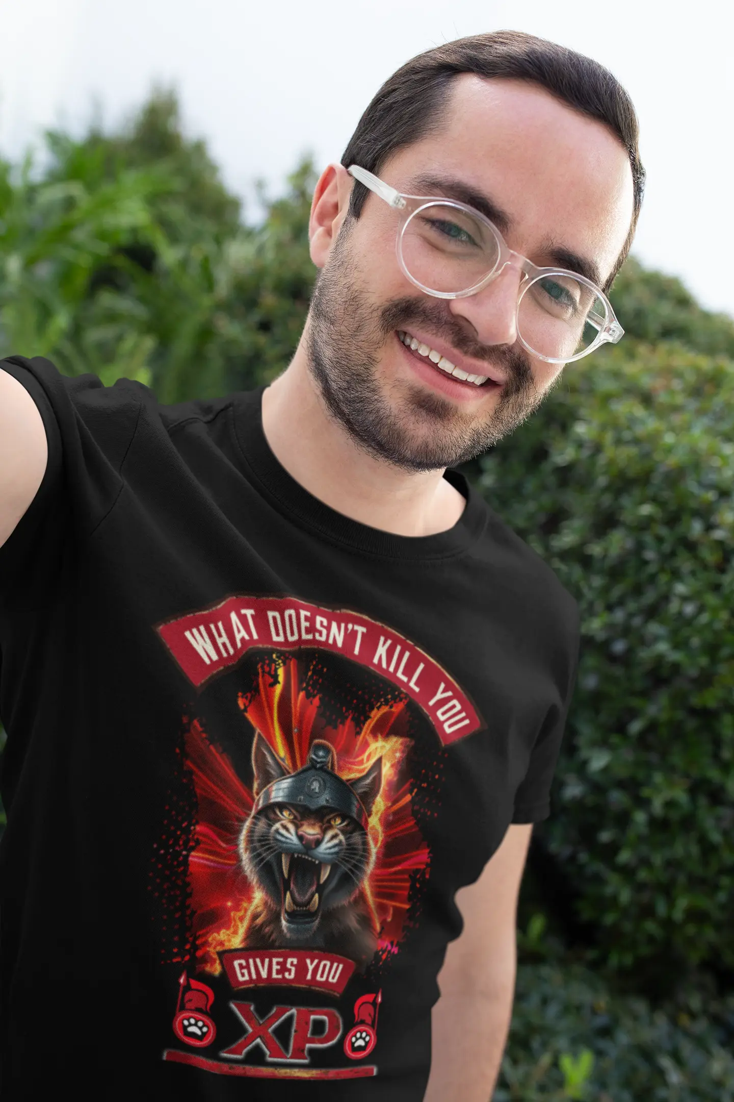 Smiling young person wearing the black Felinamia t-shirt featuring the Spartan cat print and the phrase "What Doesn't Kill You Gives You XP", showing the garment's fit in a casual setting.