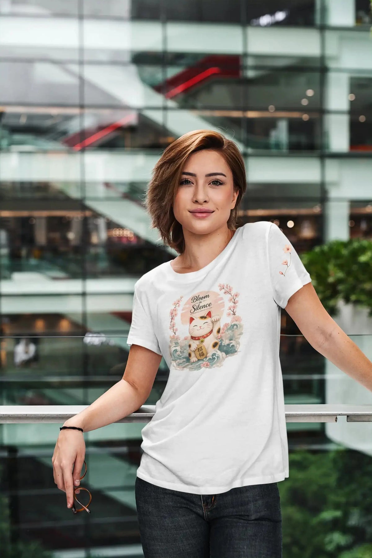 Person wearing the Bloom in Silence t-shirt in a peaceful spring garden surrounded by cherry blossoms. The Maneki Neko, Japanese waves, and sakura artwork evokes serenity, personal growth, and prosperity inspired by Japanese culture.